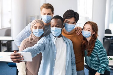 Uluslararası öğrenciler tıbbi maskeler takıp selfie çekiyorlar.