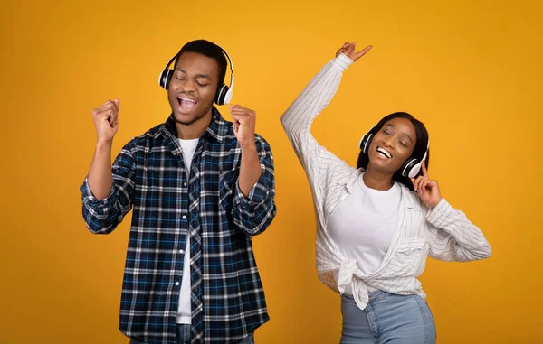 Gelukkig jong Afrikaans Amerikaans man en vrouw in casual en koptelefoon dansen en zingen op favoriete muziek — Stockfoto