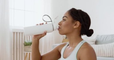 Spor ve su kaybı. Evdeki antrenmandan sonra su içen Afrikalı Amerikalı genç bir kadının portresini yakın plan çek.
