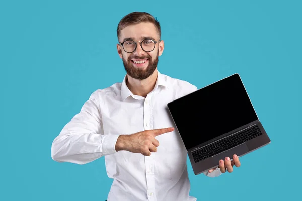 Feliz hombre de negocios milenario apuntando a la computadora portátil con maqueta para el diseño del sitio web en fondo de estudio azul —  Fotos de Stock