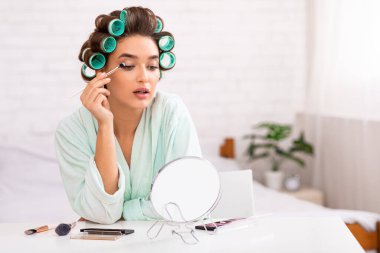 Kirpiklerine masaj yapan güzel bir kadın. Aynanın karşısında oturuyor.