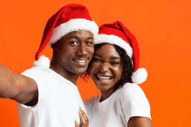 Noel Baba şapkalı güzel siyah adam ve kadın selfie çekiyorlar.
