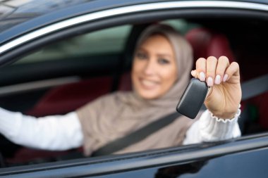 Müslüman kadın araba anahtarı gösteriyor, sürücü koltuğunda oturuyor.