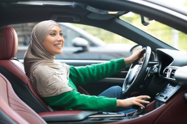 Gülümseyen Müslüman kadın şehirde yeni arabasını kullanıyor.