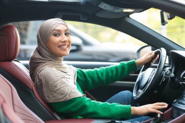 Gülümseyen Müslüman kadın yeni arabasını kullanıyor.