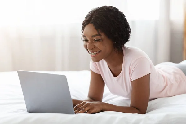 Mutlu siyah kadın yatakta dizüstü bilgisayarda flört ediyor. — Stok fotoğraf