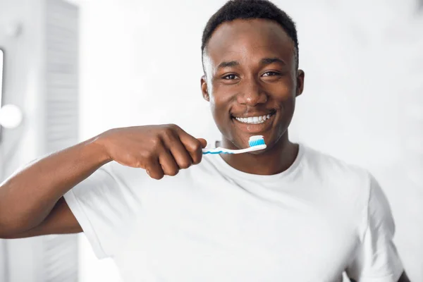 Feliz hombre afroamericano limpiando dientes de pie en el baño — Foto de Stock