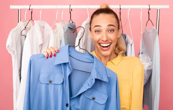 Portrait of cheerful lady showing clothes standing near rack — Stock Photo, Image