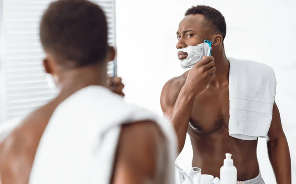 Póló nélküli fekete fickó borotválkozás arc reggel állva a fürdőszobában — Stock Fotó