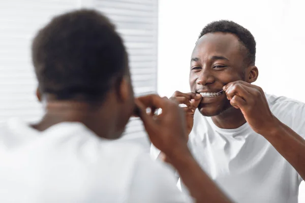Hombre africano dentado que hace fluir los dientes usando hilo dental de pie en el baño — Foto de Stock