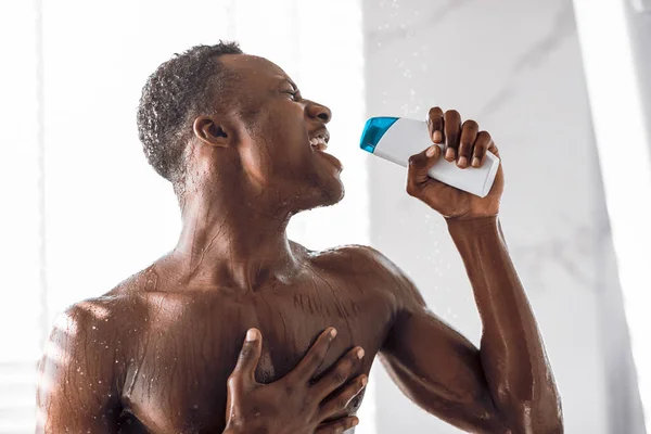 Schwarzer Mann singt in Dusche mit Shampoo-Flasche wie Mikrofon — Stockfoto