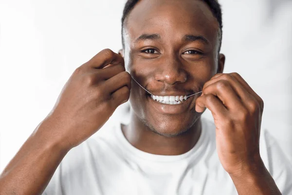 Feliz hombre negro que hace fluir los dientes usando hilo dental en el baño — Foto de Stock