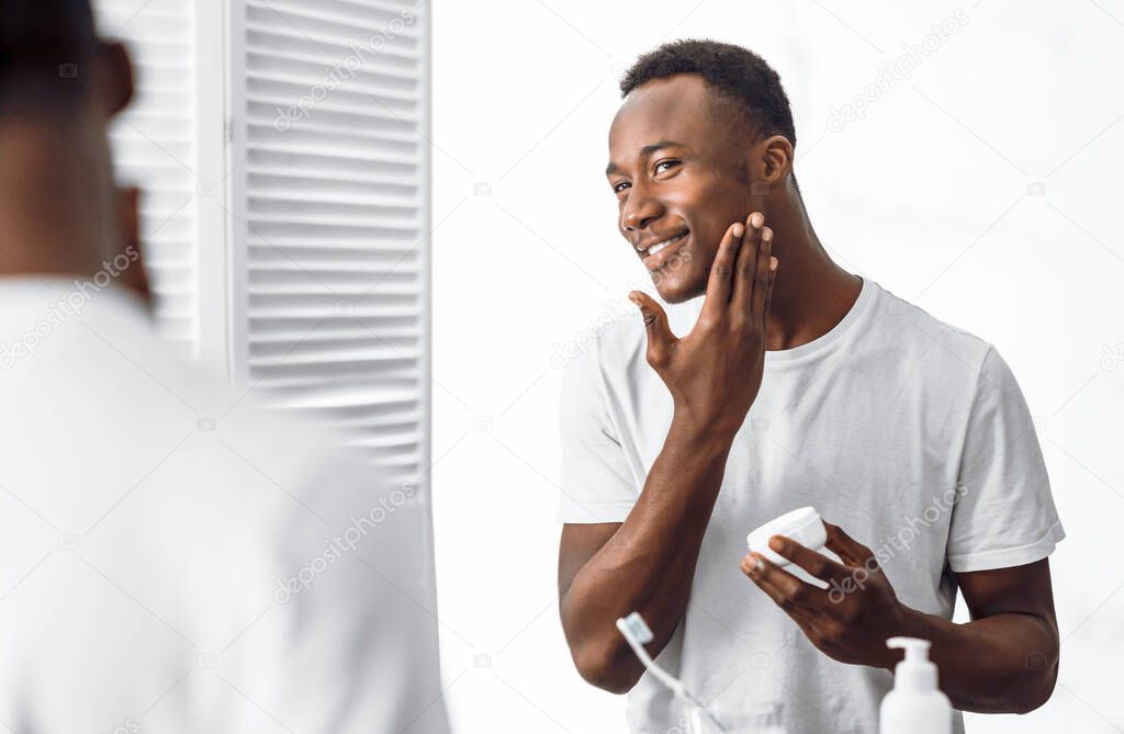Black Man Using Facial Cream Moisturizing Face Skin In Bathroom