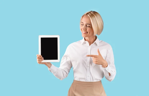Starší obchodní dáma ukazuje na tablet počítač s prázdnou obrazovkou na modrém pozadí studia, maketa pro design webových stránek — Stock fotografie