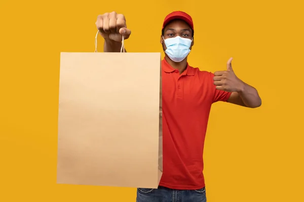 Black delivery man in medical mask holding package showing like — Stock Photo, Image