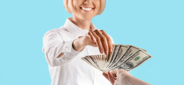 Vista recortada de la mano femenina dando dinero a la mujer de negocios en fondo de estudio azul, primer plano de las manos — Foto de Stock