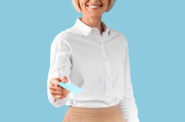 Ausgeschnittene Ansicht einer lächelnden Geschäftsfrau, die eine leere Visitenkarte mit Design-Attrappe auf blauem Studiohintergrund gibt — Stockfoto