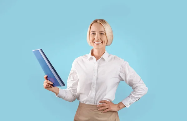 Портрет позитивної жінки-підприємця в офісному вбранні, що тримає папку з документами на синьому фоні студії — стокове фото