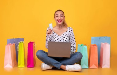 Alışveriş torbaları, dizüstü bilgisayarı ve plastik kartı olan mutlu bir kadın.