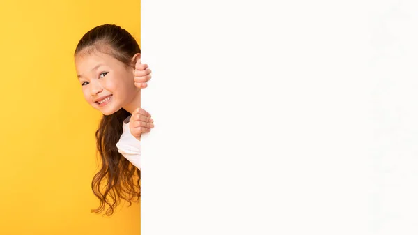 Niño asiático escondido detrás de la cartelera de publicidad blanca en blanco — Foto de Stock