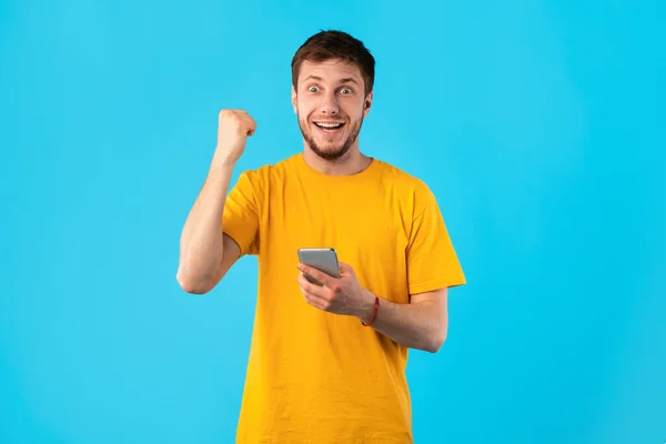 Захоплений чоловік використовує мобільний телефон на студії, святкуючи онлайн-перемогу — стокове фото