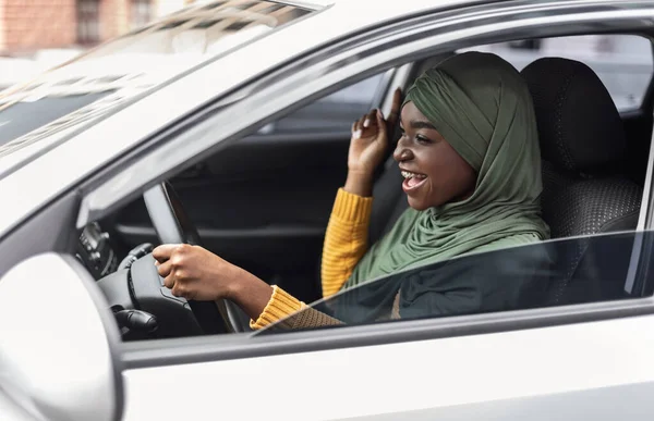 Diversión al volante. Alegre mujer musulmana negra escuchando música y cantando en coche — Foto de Stock