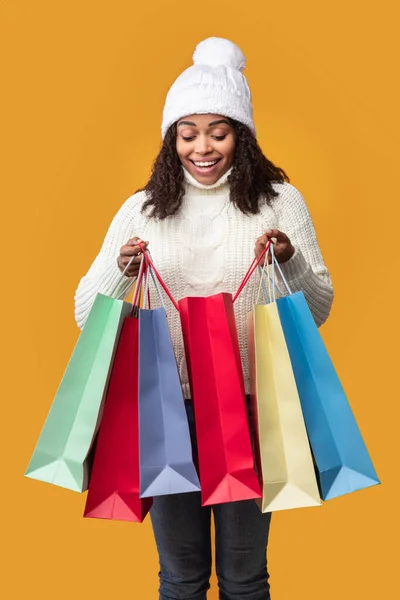 Emocionada dama negra sosteniendo bolsas de compras mirando dentro —  Fotos de Stock