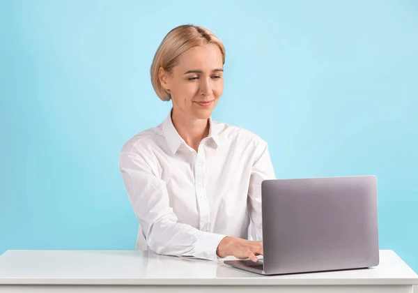 Pozitivní zralé podnikatelka pracující s notebookem na stole přes modré studio pozadí, volné místo — Stock fotografie