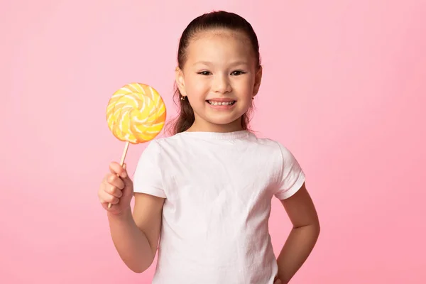 Adorable chica asiática sonriendo y sosteniendo colorida piruleta — Foto de Stock