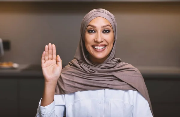 Muslim Woman Waving Hello Smiling To Camera Sitting In Kitchen — Stok Foto