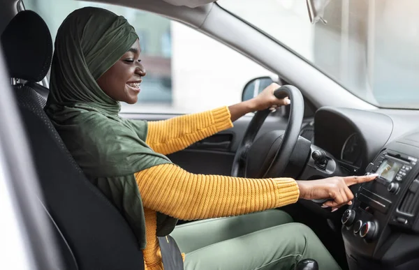 Vrolijke Afrikaanse moslim vrouw veranderen van radiostation tijdens het luisteren naar muziek in de auto — Stockfoto