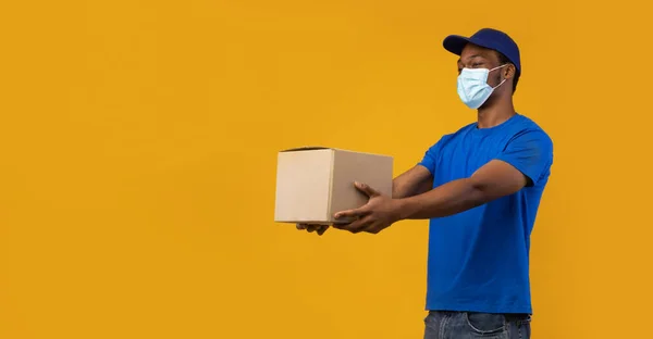 Afroamericano repartidor en máscara médica dando caja de cartón —  Fotos de Stock