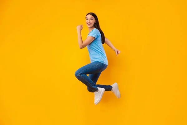 Щаслива жінка стрибає через жовту стіну студії — стокове фото