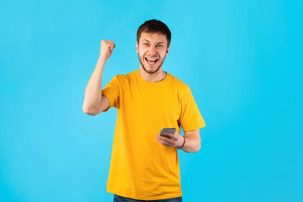 Homem animado usando telefone celular no estúdio, comemorando a vitória — Fotografia de Stock