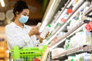 Akıllı telefon kullanan maskeli Afrikalı kadın dükkandan alışveriş yapıyor.