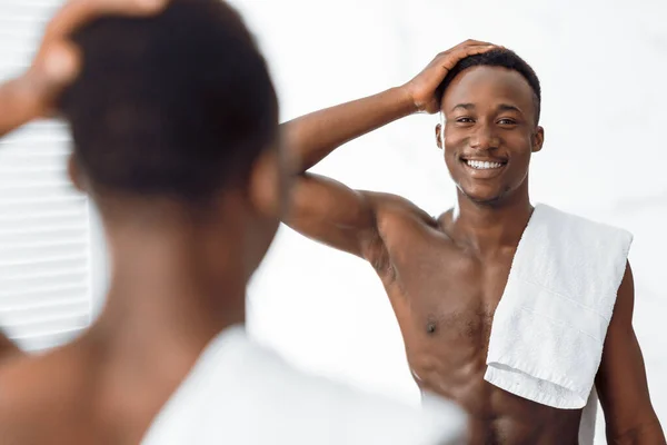 アフリカ系アメリカ人の男性がモダンなバスルームに立つ髪に触れる — ストック写真