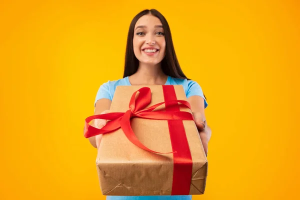 Happy woman holding gift box at studio, giving to camera — Stock fotografie