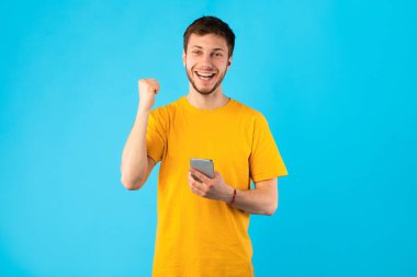 Stüdyoda akıllı telefon kullanan heyecanlı adam, online zaferi kutluyor.