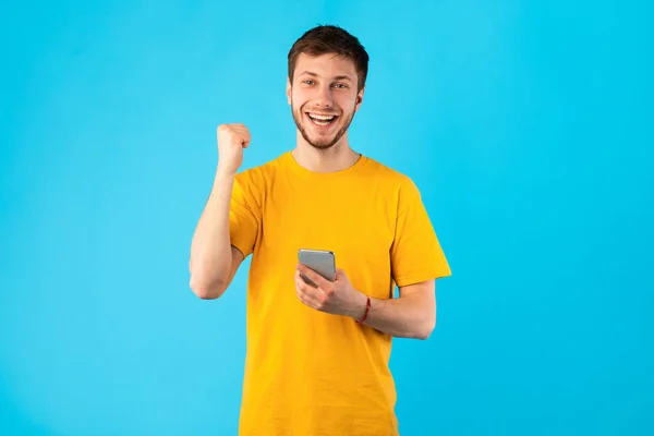 Opgewonden man met behulp van smartphone in de studio, het vieren van online winnen — Stockfoto