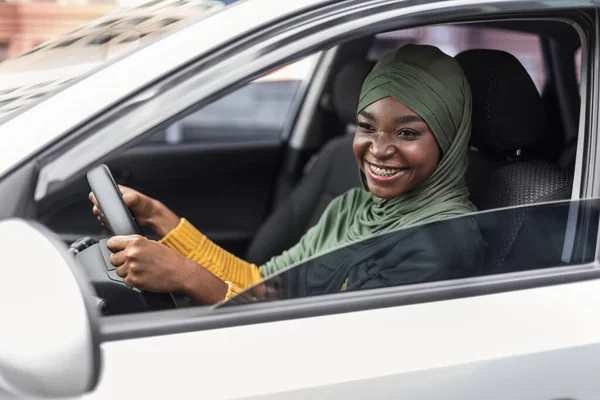 새 차를 운전하는 즐거움을 주는 머리 스카프를 두른 행복 한 젊은 흑인 모슬렘 여인 — 스톡 사진
