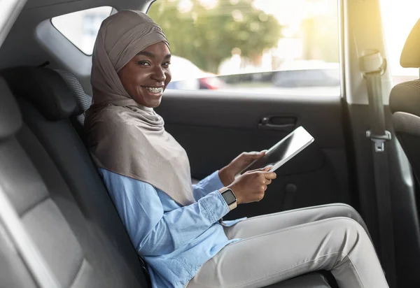 Cherful zwarte vrouw in hidjab met behulp van digitale tablet op de achterbank in de auto — Stockfoto