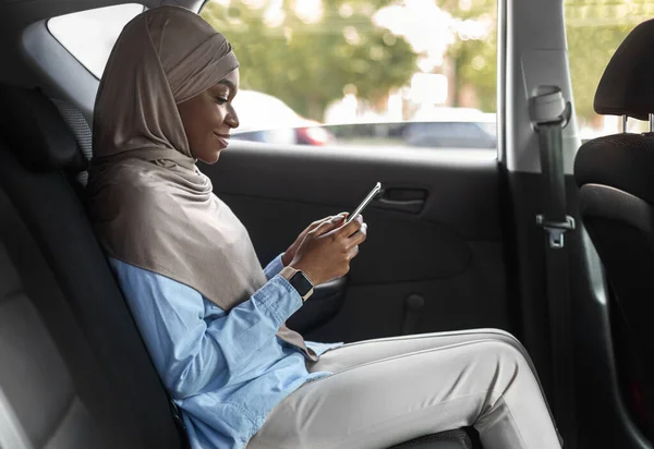 Lachende zwarte moslim vrouwelijke ondernemer Browsing Smartphone tijdens het rijden auto op de achterbank — Stockfoto