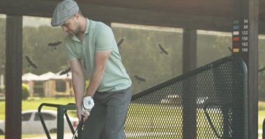 Genç konsantre olmuş bir adam demirle topa vuruyor, özel bir kulüpte golf oynuyor.