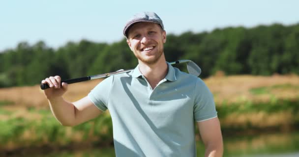 Potret luar ruangan pria berjanggut muda berpose dengan tongkat golf, tersenyum ke kamera, pelacakan tembakan — Stok Video