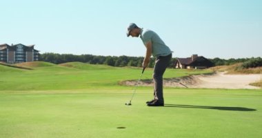 Konsantre golf oyuncusu topa delikten vuruyor, dışarıda golf oynuyor.