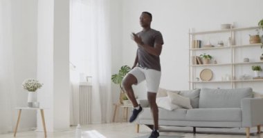 Genç Afrikalı Amerikalı adam evde enerjik bir şekilde koşuyor, iç kardiyo eğitimi alıyor.