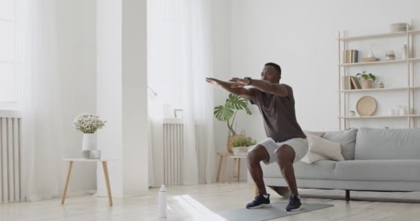 Treino caseiro. Jovem esportivo afro-americano fazendo exercícios de agachamento, treinamento esportivo sozinho — Vídeo de Stock