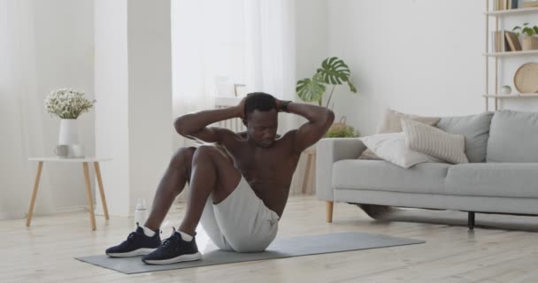 Афроамериканец без рубашки делает упражнения по перекрёстному перекрестку, лежа на полу дома — стоковое видео