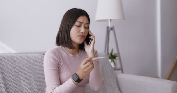 高熱で苦しんでいる若いアジアの女性インフルエンザや風邪の治療について電話で医師と相談する — ストック動画