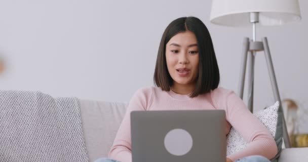 ラップトップ画面を見ている若いアジアの女性は、コンピュータでオンラインニュースを見て興奮し、個人的な販売を得ました — ストック動画